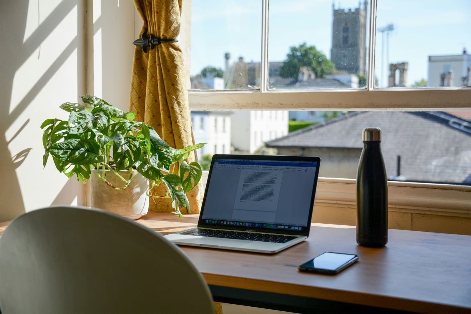 Schreibtisch am Fenster mit Laptop, Zimmerpflanze und Trinkflasche